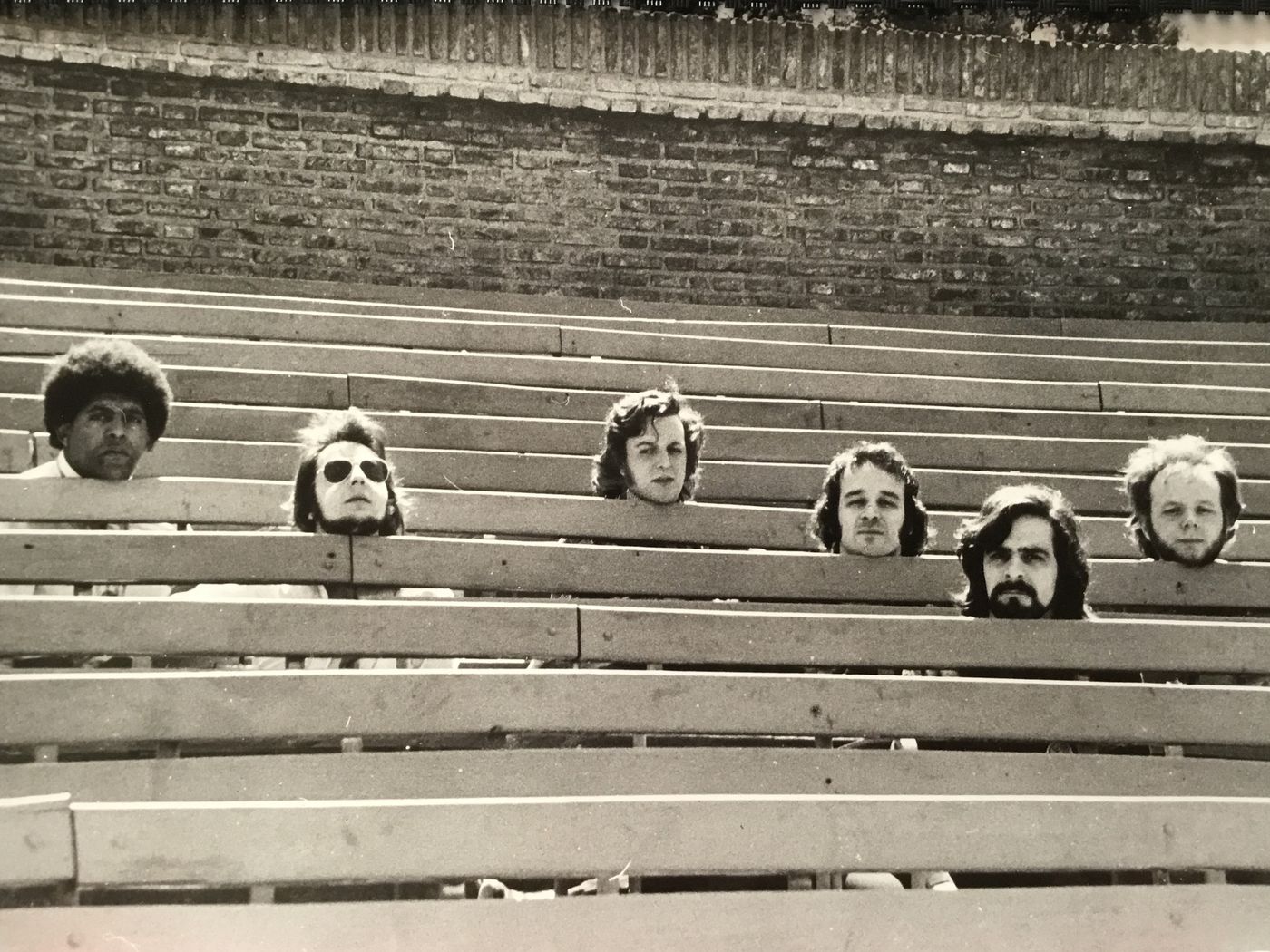 The six members of S.O.S. peering over the rows of an empty wooden grandstand: Rubén Rada far left, Luis Ceravolo beside him.